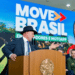 Presidente discursando com chapéu em evento Move Brasil, painel destaca entregador e entregadora sorrindo ao fundo