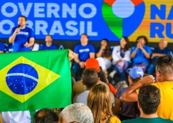 Pessoas assistem a evento do Governo do Brasil, com painel azul, bandeira nacional e participantes no palco
