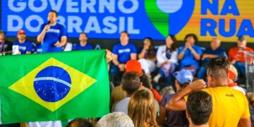 Pessoas assistem a evento do Governo do Brasil, com painel azul, bandeira nacional e participantes no palco