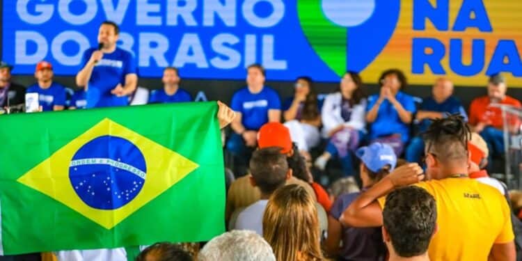 Pessoas assistem a evento do Governo do Brasil, com painel azul, bandeira nacional e participantes no palco