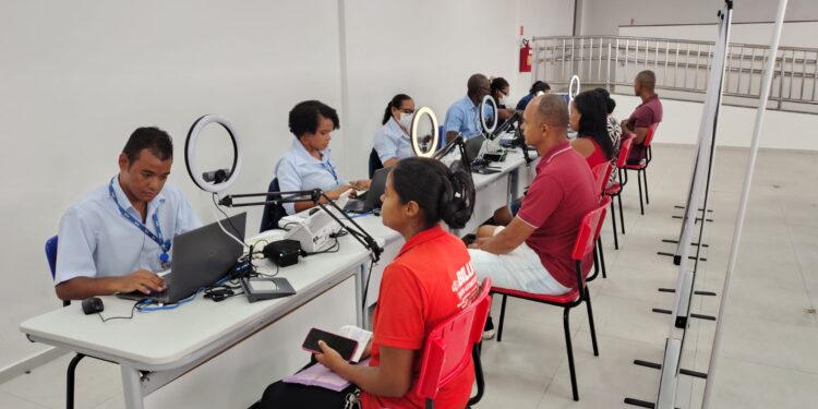 Atendentes do SAC com uniformes azuis atendem cidadãos para emissão da nova CIN em espaço com ring lights e notebooks