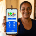 Mulher sorridente segura celular mostrando tela do app Bolsa Família com calendário e opções de saque