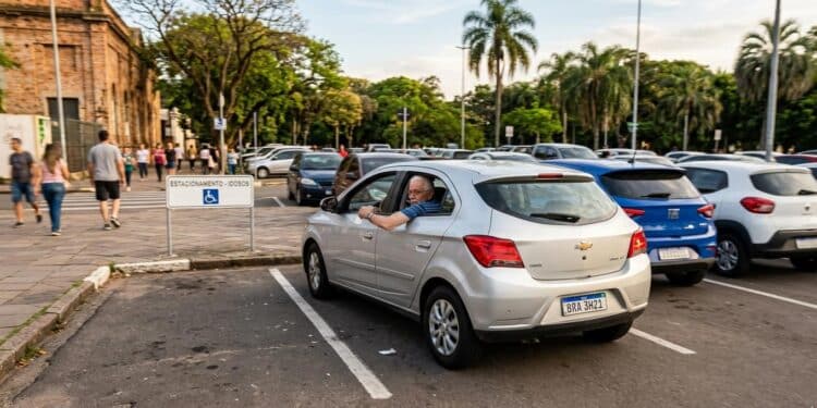 Homem idoso em Chevrolet Onix prata estaciona em vaga exclusiva para idosos com placa "ESTACIONAMENTO - IDOSOS"