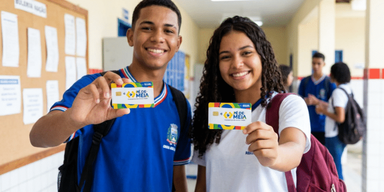 Jovens estudantes sorrindo exibem cartões do Pé-de-Meia em corredor de escola, com uniformes azul e branco