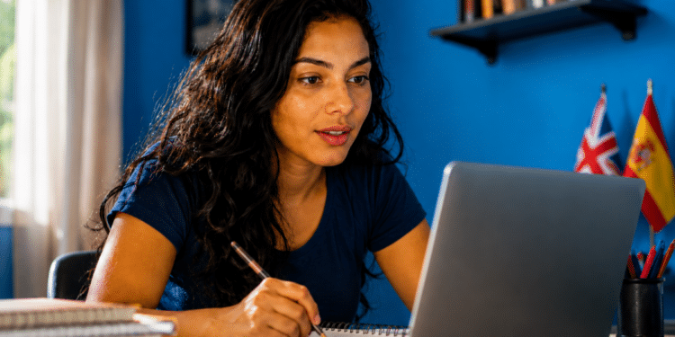 Jovem estuda idioma em casa pelo notebook com bandeiras do Reino Unido e da Espanha ao lado