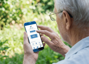 Homem idoso de cabelos brancos usando óculos e camisa cinza interage com celular mostrando app Meu INSS em área externa