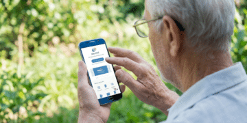 Homem idoso de cabelos brancos usando óculos e camisa cinza interage com celular mostrando app Meu INSS em área externa