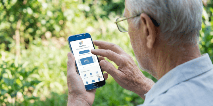 Homem idoso de cabelos brancos usando óculos e camisa cinza interage com celular mostrando app Meu INSS em área externa