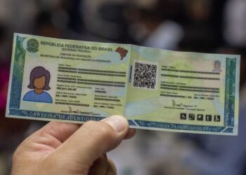 Mão segurando nova Carteira de Identidade Nacional brasileira, fundo difuso e dados fictícios.