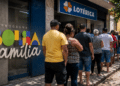 Pessoas em fila na porta de uma lotérica ao lado do letreiro Bolsa Família em ambiente urbano