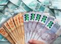 Notas de 50, 100 e 200 reais brasileiras em leque sobre fundo de dinheiro espalhado