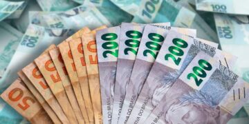 Notas de 50, 100 e 200 reais brasileiras em leque sobre fundo de dinheiro espalhado