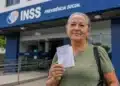 Beneficiária segura documento em frente a uma agência do INSS, representando o anúncio de R$ 547 milhões para ressarcimentos.