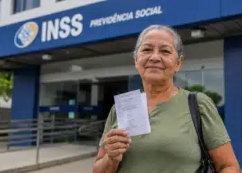 Beneficiária segura documento em frente a uma agência do INSS, representando o anúncio de R$ 547 milhões para ressarcimentos.