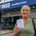 Beneficiária segura documento em frente a uma agência do INSS, representando o anúncio de R$ 547 milhões para ressarcimentos.