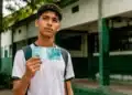 Estudante segurando nota de cem reais em frente a uma escola pública, representando o próximo pagamento do programa Pé-de-Meia.