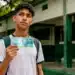 Quando o Pé-de-Meia volta a cair? Veja a data do próximo pagamento aos estudantes 13 Estudante segurando nota de cem reais em frente a uma escola pública, representando o próximo pagamento do programa Pé-de-Meia.