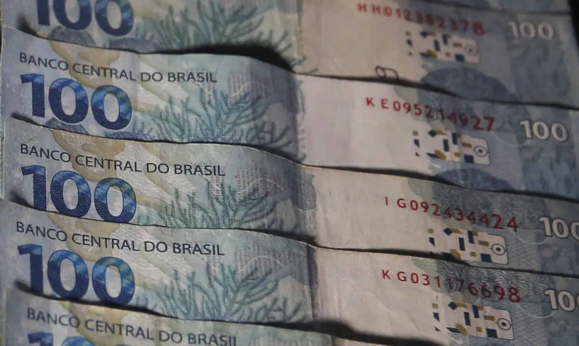 Cédulas de cem reais do Banco Central do Brasil enfileiradas, representando o crédito e a renegociação de dívidas dos programas do governo
