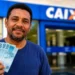Trabalhador segura notas de R$ 100 em frente a uma agência da Caixa, representando a distribuição do lucro do FGTS.