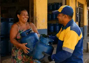 Mulher retirando um botijão de gás do programa Gás do Povo em uma revenda durante o atendimento, representando a liberação do benefício em julho de 2026.