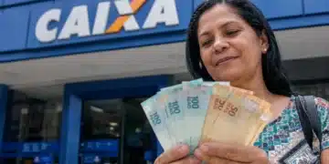 Mulher segura cédulas de real em frente a uma agência da Caixa, representando as novas liberações do Saque Calamidade do FGTS.