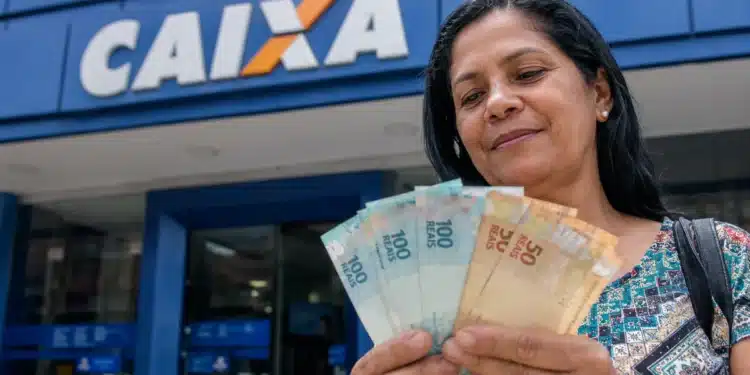 Mulher segura cédulas de real em frente a uma agência da Caixa, representando as novas liberações do Saque Calamidade do FGTS.
