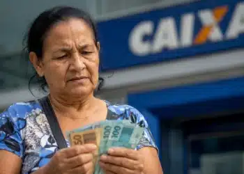 Beneficiária confere dinheiro em frente a uma agência da Caixa, representando os pagamentos do INSS de julho, que começam nesta segunda-feira, 27.