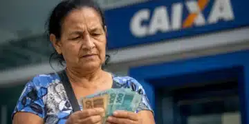 Beneficiária confere dinheiro em frente a uma agência da Caixa, representando os pagamentos do INSS de julho, que começam nesta segunda-feira, 27.