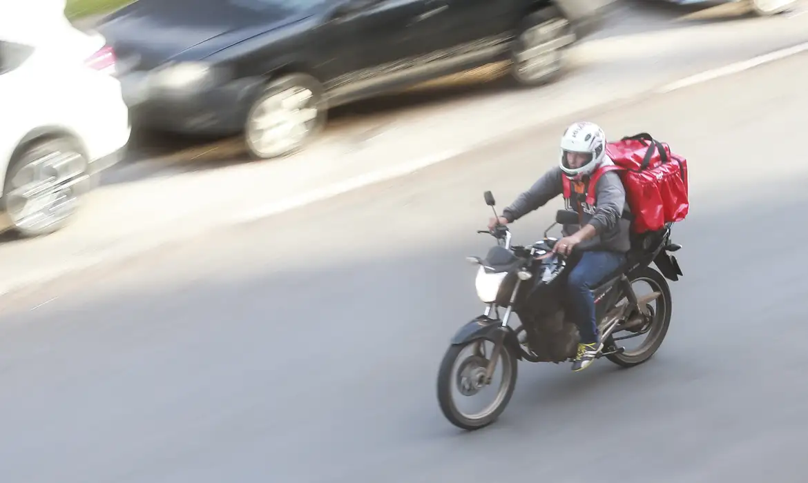 Motoboy conduz moto com baú de entregas em avenida, perfil de trabalhador atendido pelo crédito sem entrada do Move Brasil