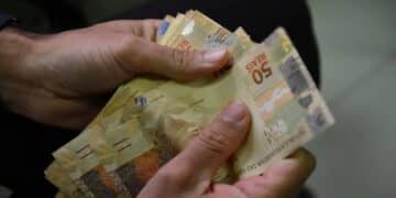 Mãos contam cédulas de cinquenta reais, ilustrando os programas do governo para renegociar dívidas e liberar crédito