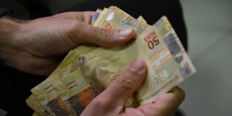 Mãos contam cédulas de cinquenta reais, ilustrando os programas do governo para renegociar dívidas e liberar crédito