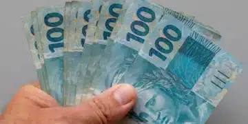 Mão segura cédulas de R$ 100, representando a solicitação do Saque Calamidade de até R$ 6.220, liberado pela Caixa.