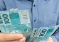 Trabalhador segurando notas de reais, representando os valores do lucro do FGTS em 2026.