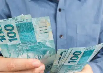 Trabalhador segurando notas de reais, representando os valores do lucro do FGTS em 2026.