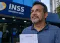 Homem segura receituário médico em frente a unidade do INSS, representando auxílio por doença grave sem carência.