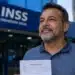 Homem segura receituário médico em frente a unidade do INSS, representando auxílio por doença grave sem carência.