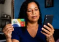 Beneficiária consulta informações do Bolsa Família pelo celular enquanto segura cartão do programa