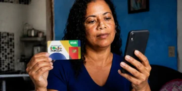 Beneficiária consulta informações do Bolsa Família pelo celular enquanto segura cartão do programa