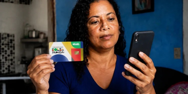 Beneficiária consulta informações do Bolsa Família pelo celular enquanto segura cartão do programa