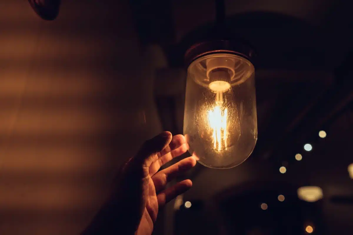 Desconto na conta de luz: 586 mil beneficiários perdem a Tarifa Social e governo cobra a Aneel 2 Mão próxima a uma lâmpada acesa, representando os critérios de acesso ao desconto na conta de energia.