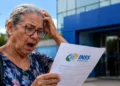 Aposentada analisa documento do INSS em frente a uma agência após encerramento do Meu INSS Vale+
