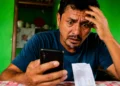 Homem preocupado consulta o celular ao receber informação sobre falso Auxílio Reconstrução de R$ 1.050.