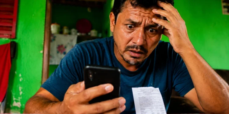 Homem preocupado consulta o celular ao receber informação sobre falso Auxílio Reconstrução de R$ 1.050.