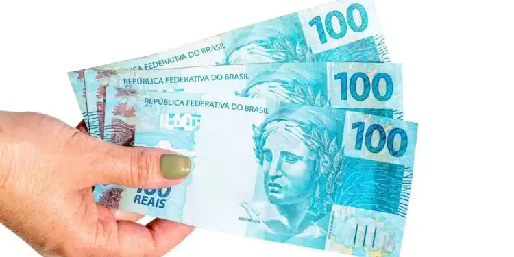 Mães de Pernambuco: Caixa deposita R$ 300 nesta sexta (7) para beneficiárias do Bolsa Família 1 Mão segurando cédulas de real representando o pagamento de R$ 300 do programa Mães de Pernambuco