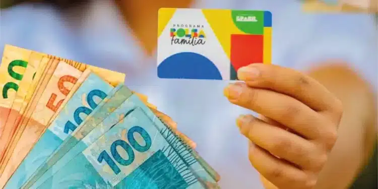 Beneficiária segura o cartão do Bolsa Família e notas de real, representando os pagamentos do benefício em agosto.