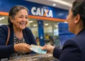 Idosa recebe dinheiro em atendimento bancário, ilustrando o pagamento dos benefícios do INSS referentes a agosto.