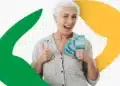 Idosa segurando cédulas de real, representando o pagamento dos benefícios do INSS em agosto a partir do dia 25.