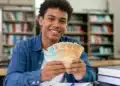 Estudante segura cédulas de real em referência ao pagamento de R$ 200 do Pé-de-Meia em agosto