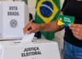 Acesso a benefícios sociais não depende de voto ou apoio político; veja esclarecimento do MDS 14 Pessoa inserindo voto em urna eletrônica enquanto segura cartão do Bolsa Família, representando o esclarecimento sobre o acesso a benefícios sociais sem relação com voto ou apoio político.