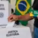 Acesso a benefícios sociais não depende de voto ou apoio político; veja esclarecimento do MDS 14 Pessoa inserindo voto em urna eletrônica enquanto segura cartão do Bolsa Família, representando o esclarecimento sobre o acesso a benefícios sociais sem relação com voto ou apoio político.